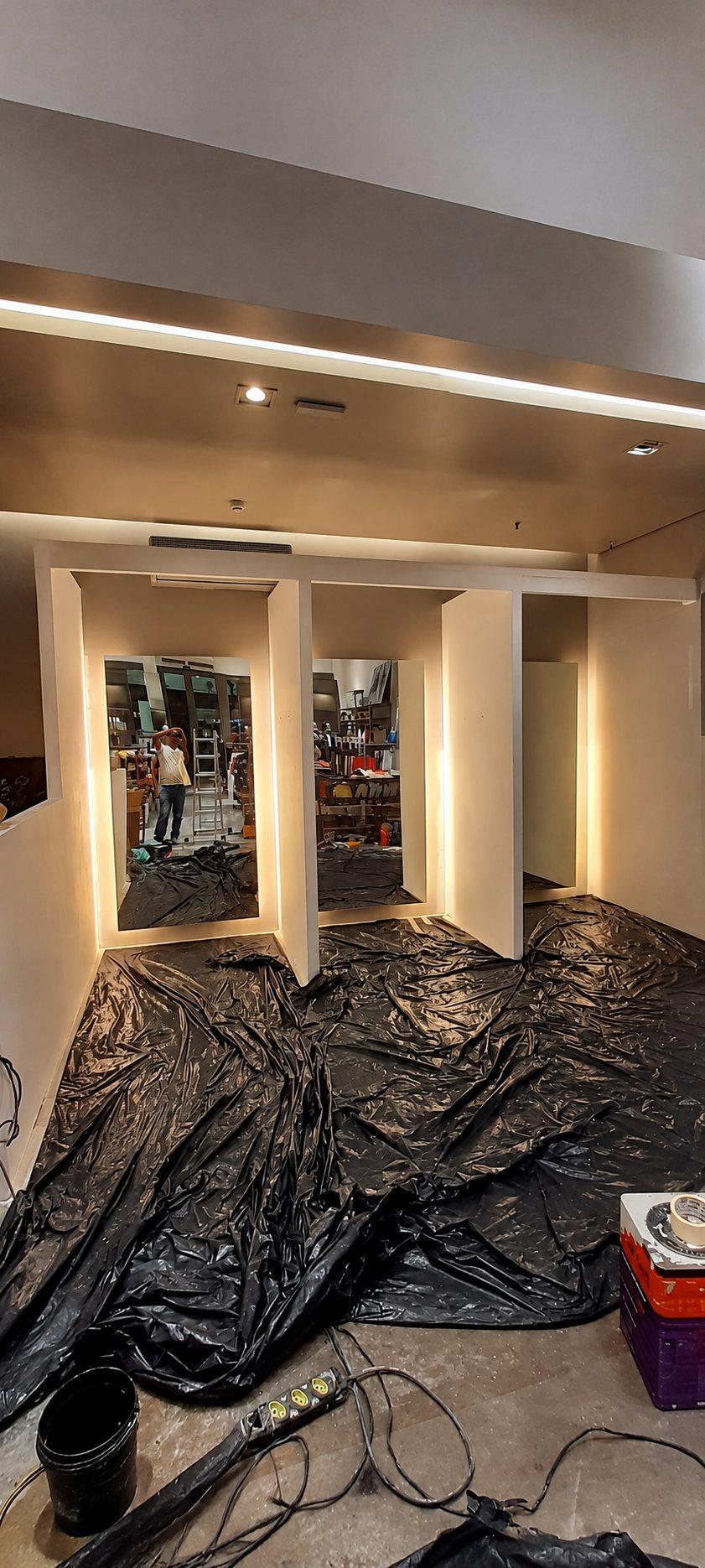 Reforma de ambiente: estrutura branca de painéis com espelhos e iluminação embutida, e o piso protegido por lona preta